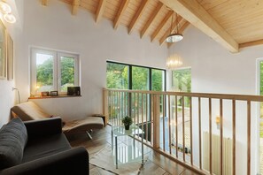 A modern interior with a sofa, a glass table, and a balcony with a wooden railing. - Holiday Home 'Eifel Atrium' with Private Terrace and Wi-Fi (Zweifelscheid)