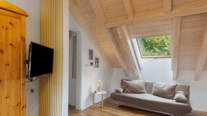 Une chambre de style loft moderne, avec un plafond en pente, un téléviseur encastré, un canapé et une fenêtre donnant sur un paysage verdoyant.