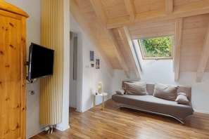 Un dormitorio tipo loft moderno con techo inclinado, televisor integrado, sofá y ventana con vistas a zonas verdes.