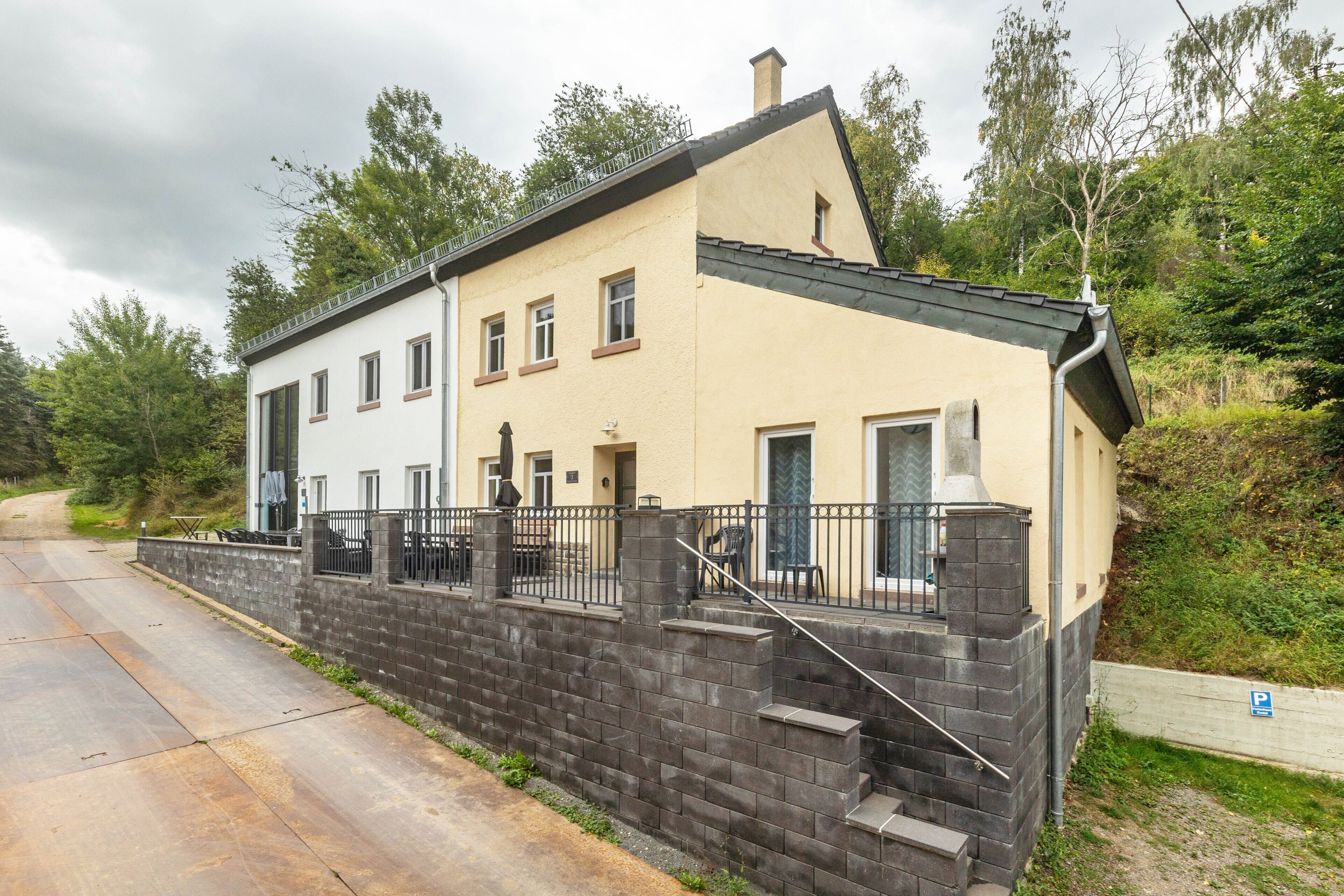 A two-story building with a stone wall and a metal fence.