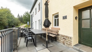 An outdoor patio with a table and chairs, a wooden bench, and a green door. - Holiday Home 'Enztal' with Shared Terrace (Zweifelscheid)