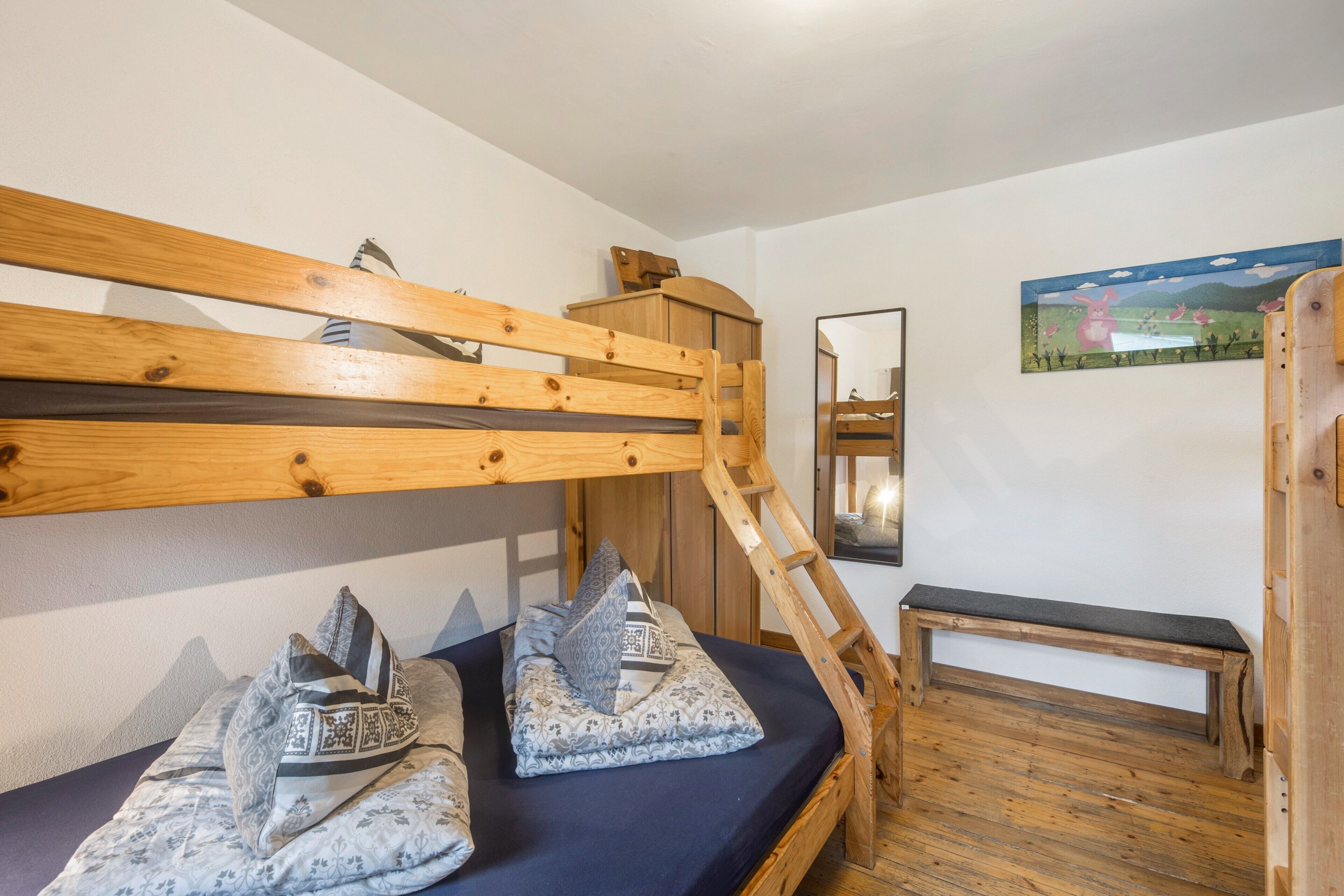 A bunk bed with a wooden ladder, a small bench, and a mirror on the wall.