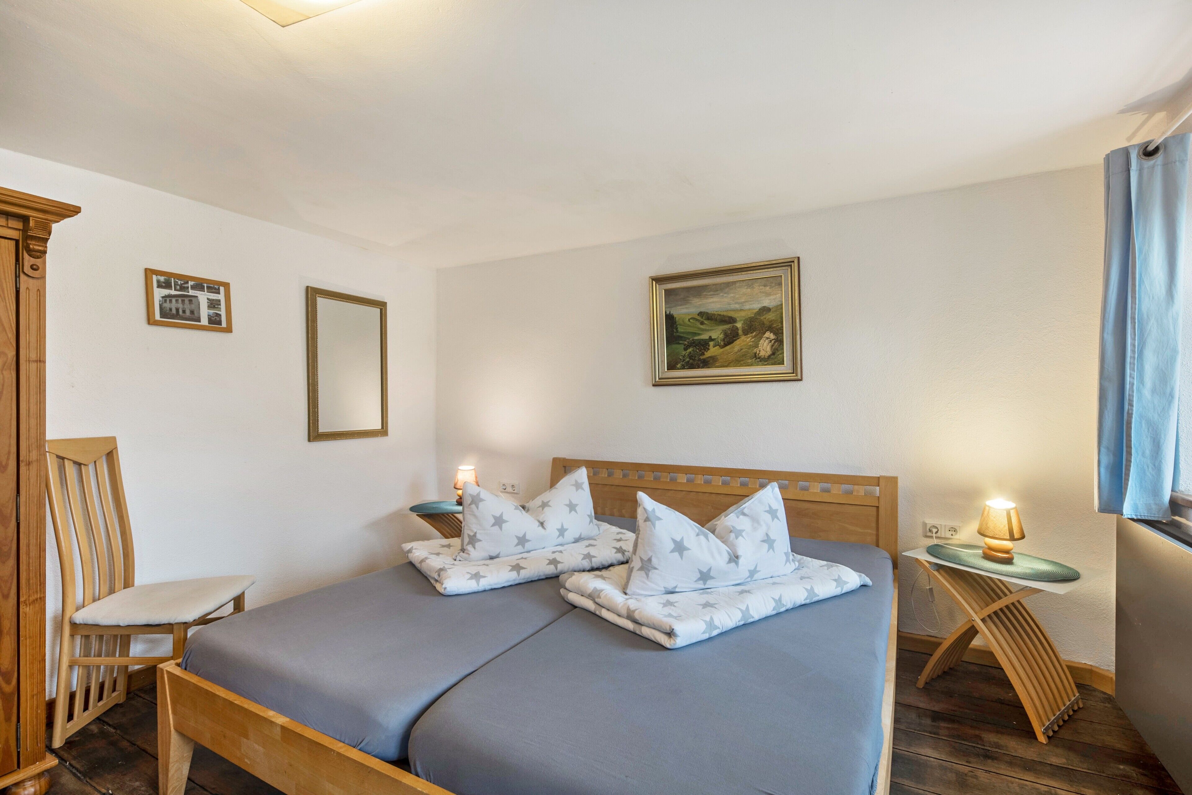 Ein Doppelbett mit Kissen mit Sternenmuster, ein Holzkopfteil, ein Nachttisch mit Lampe, ein Bilderrahmen und ein Spiegel an der Wand.