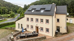 A two-story building with a flat roof, multiple windows, and a paved patio area with outdoor seating. - Holiday Home 'Eifellandhaus' with Shared Terrace and Wi-Fi (Zweifelscheid)