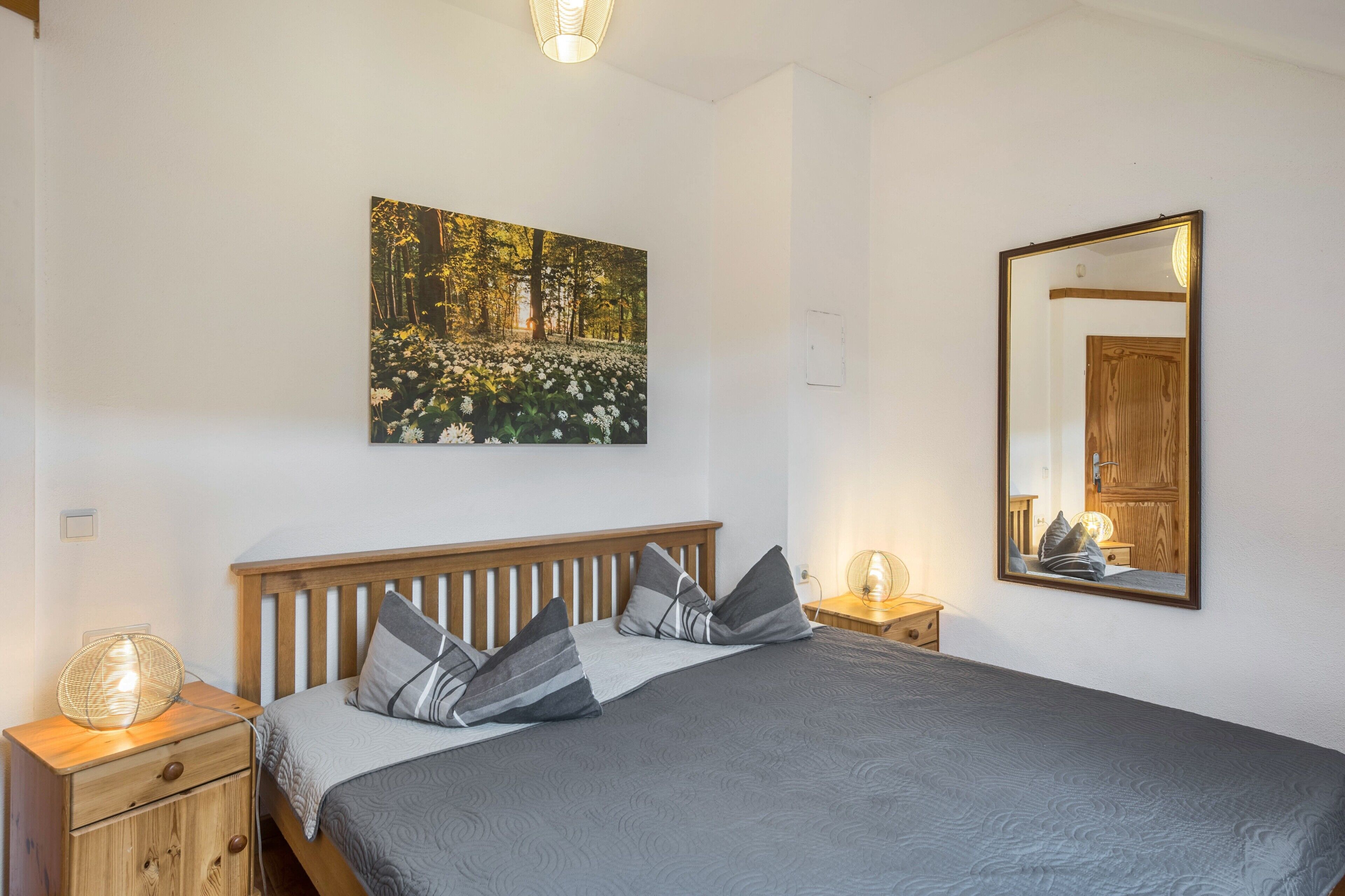 A bedroom with a bed, nightstands, a wall-mounted mirror, and a painting.