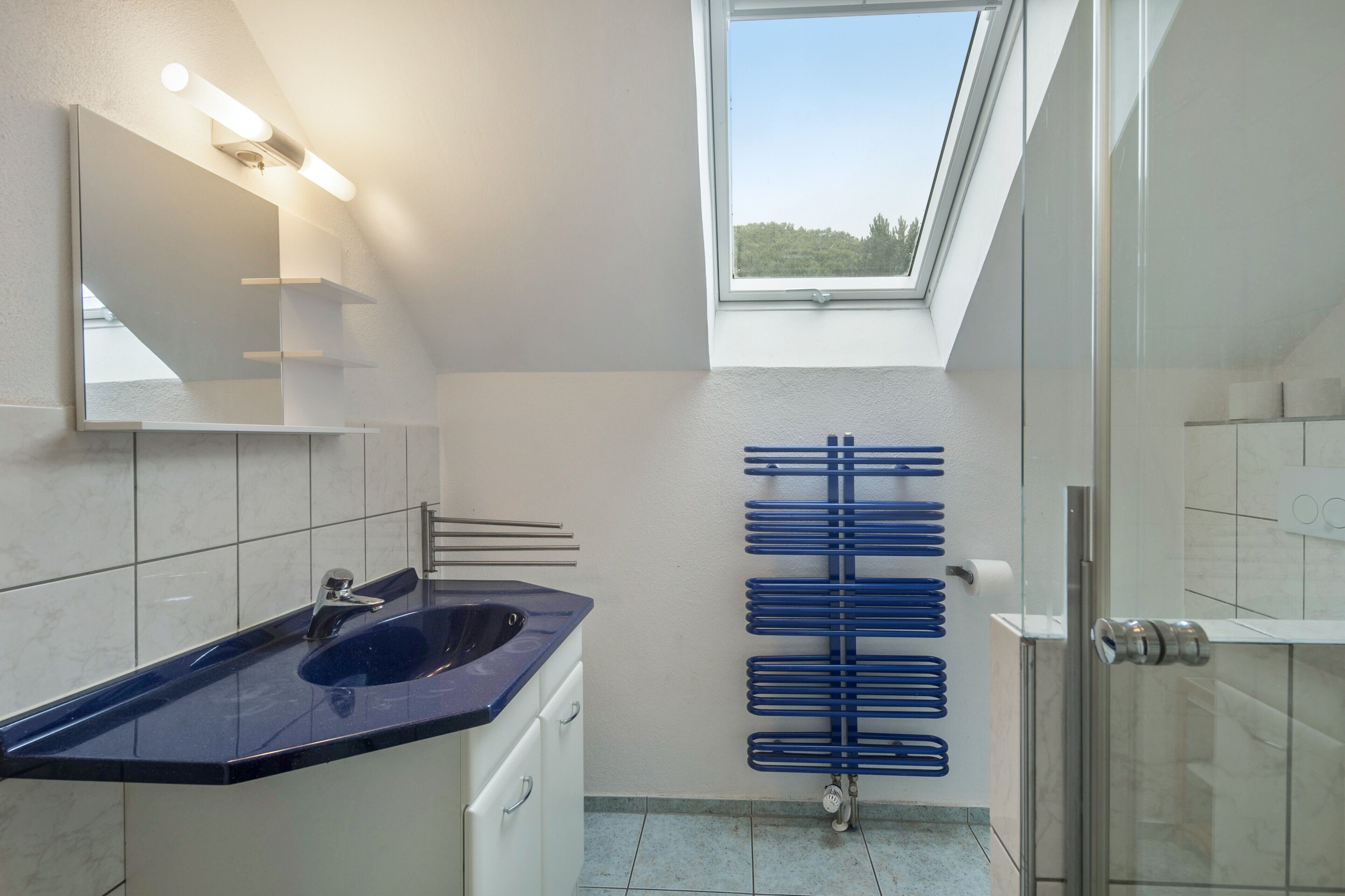 Een moderne badkamer met een dakraam, een blauwe wastafel en een handdoekhouder.