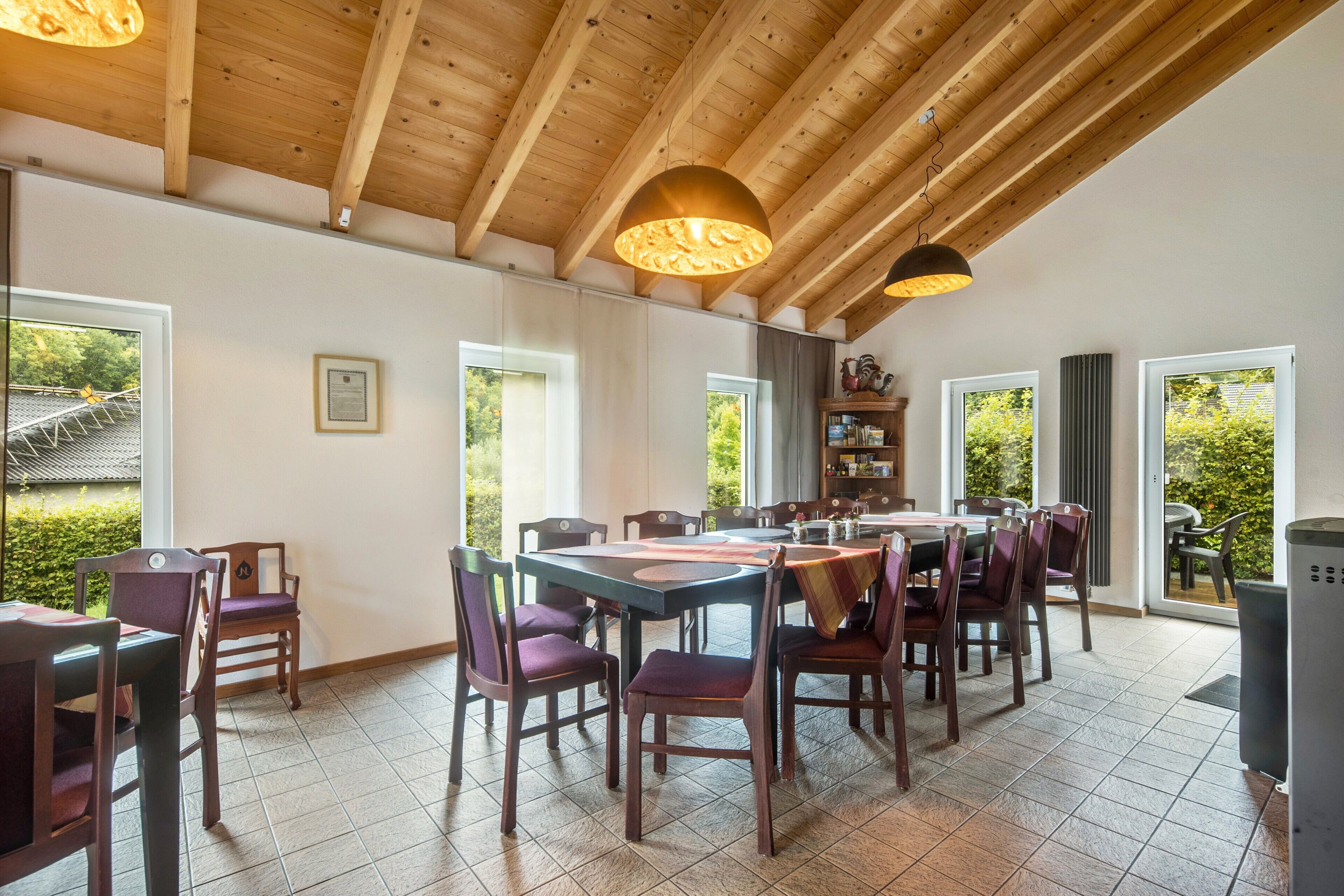 A dining area with wooden beams, large windows, and a view of greenery outside.