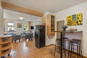 A modern kitchen with a refrigerator, wooden cabinets, and a bar area with stools.