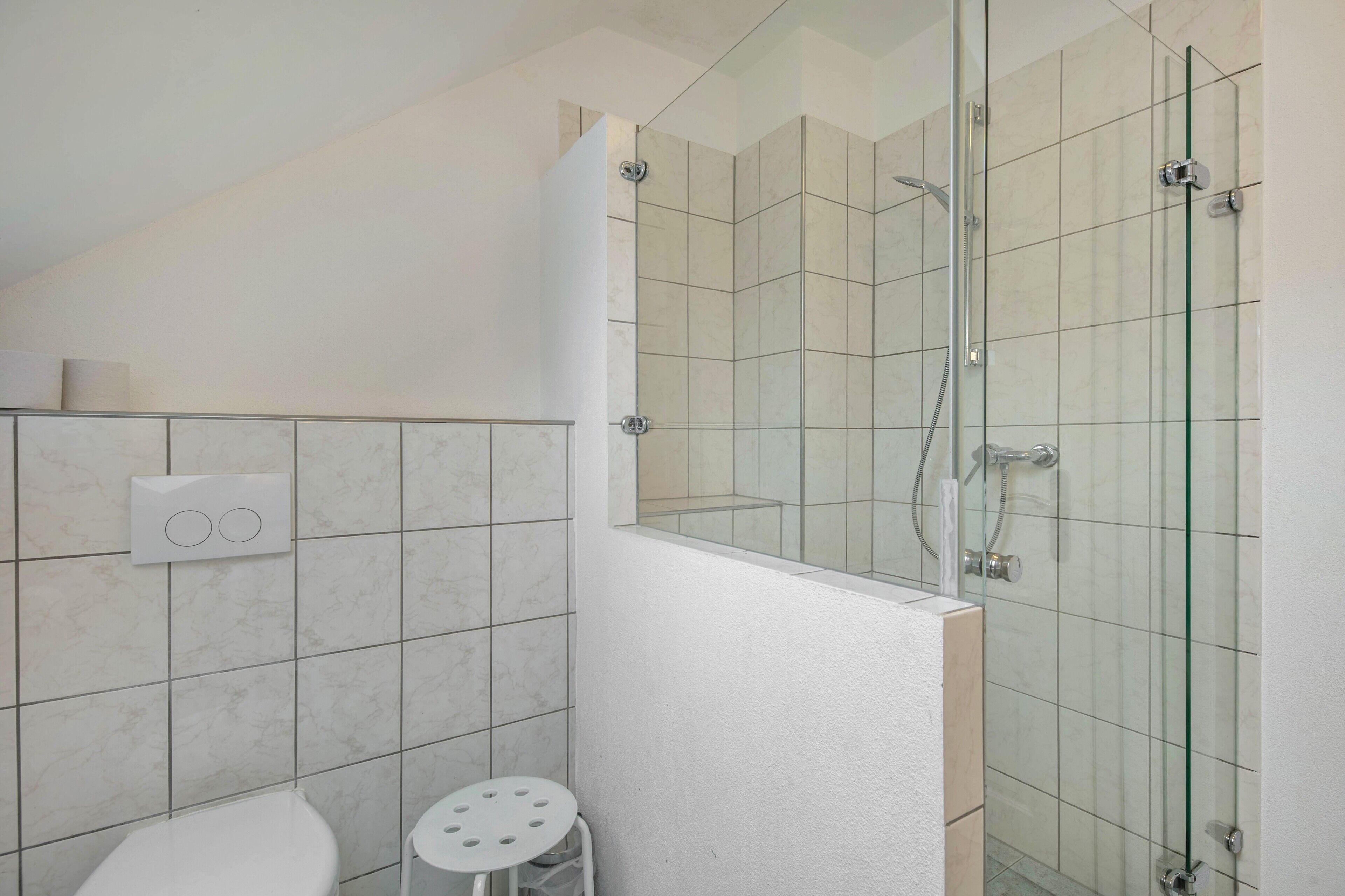A bathroom with a glass-enclosed shower, a toilet, and a small stool.