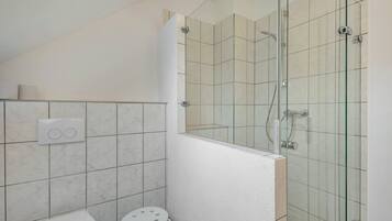 A bathroom with a glass-enclosed shower, a toilet, and a small stool.