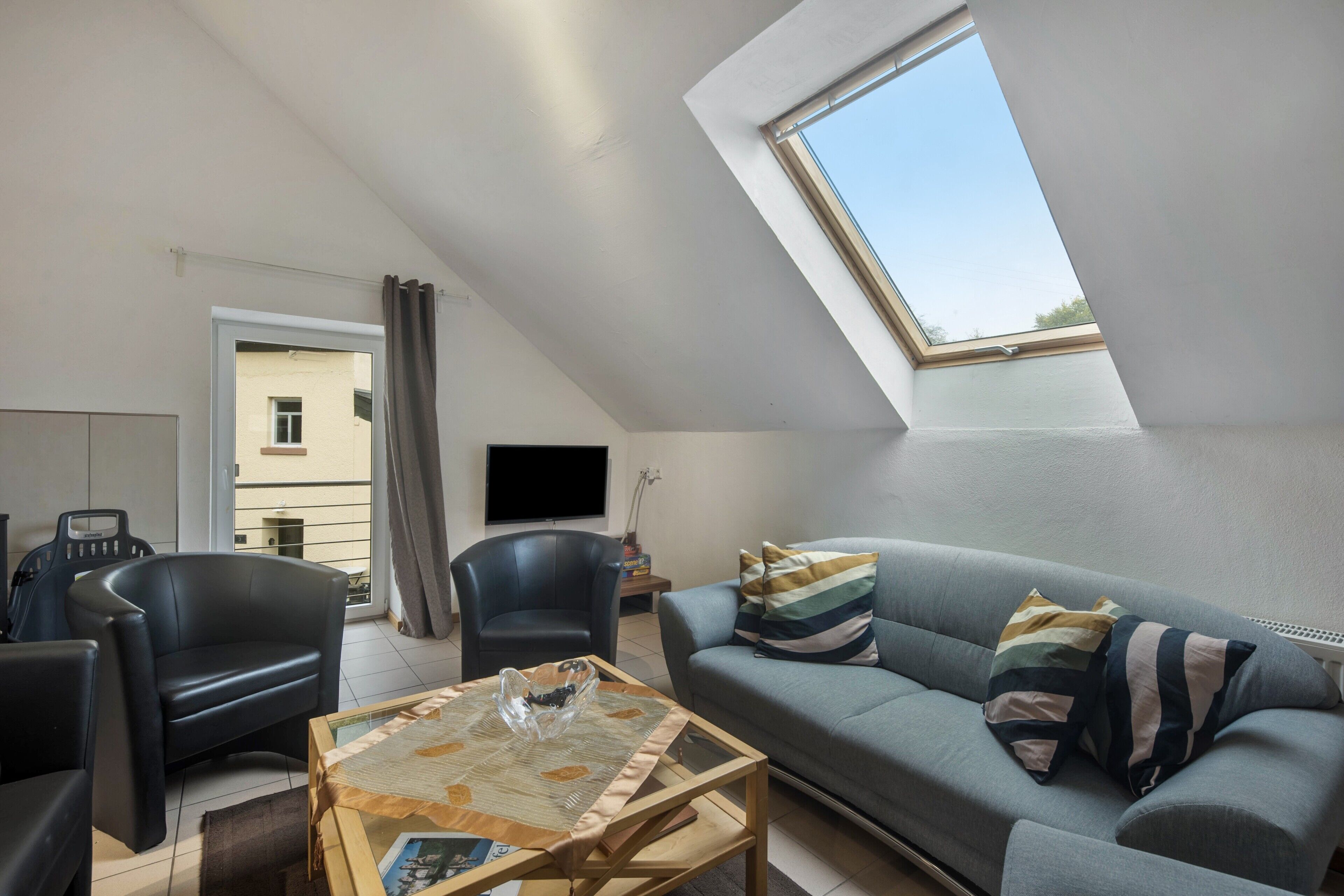 A modern living room with a sloped ceiling, a sofa, two armchairs, a coffee table, and a TV.
