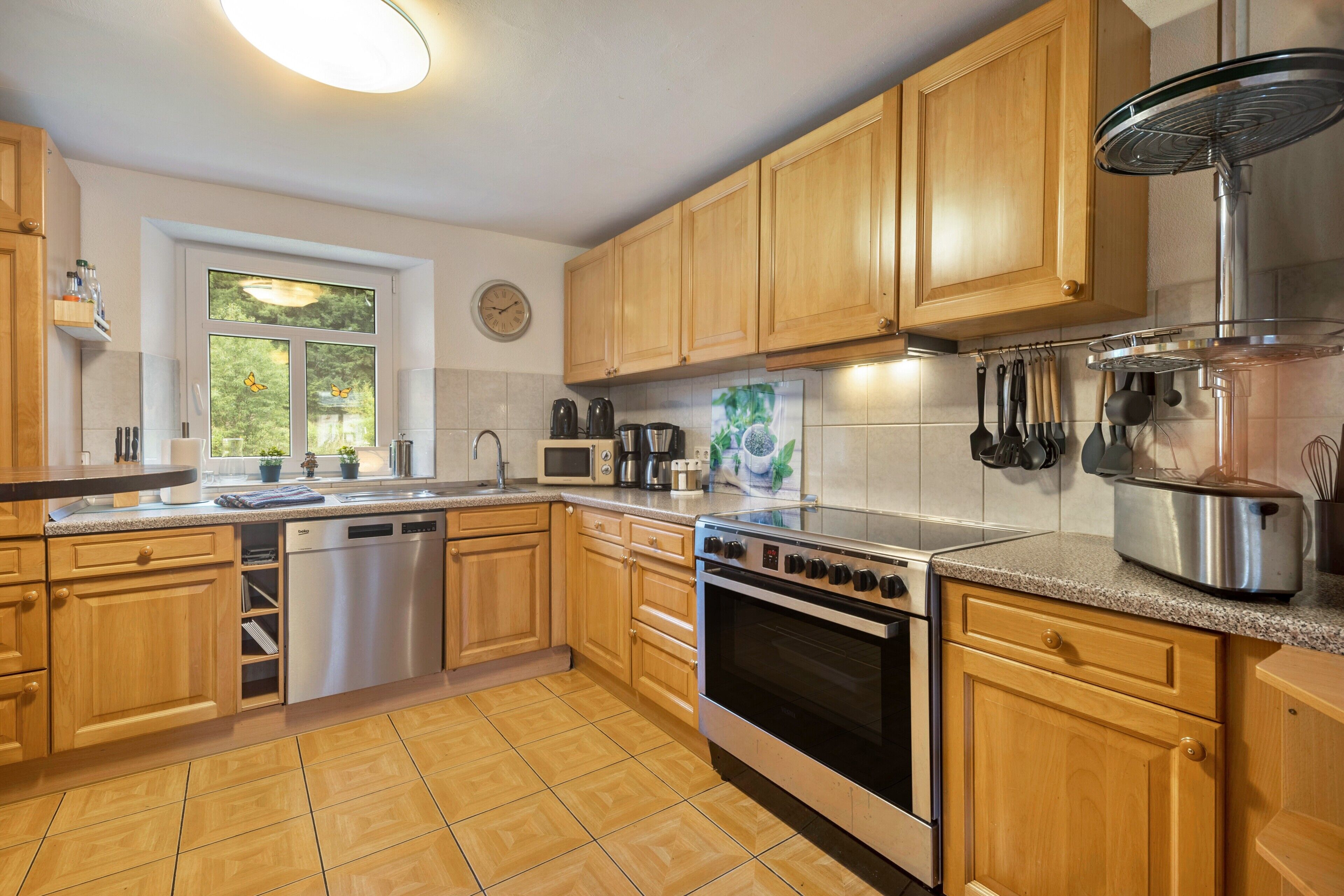 A kitchen with wooden cabinets, stainless steel appliances, a dishwasher, and a window with a view of greenery.