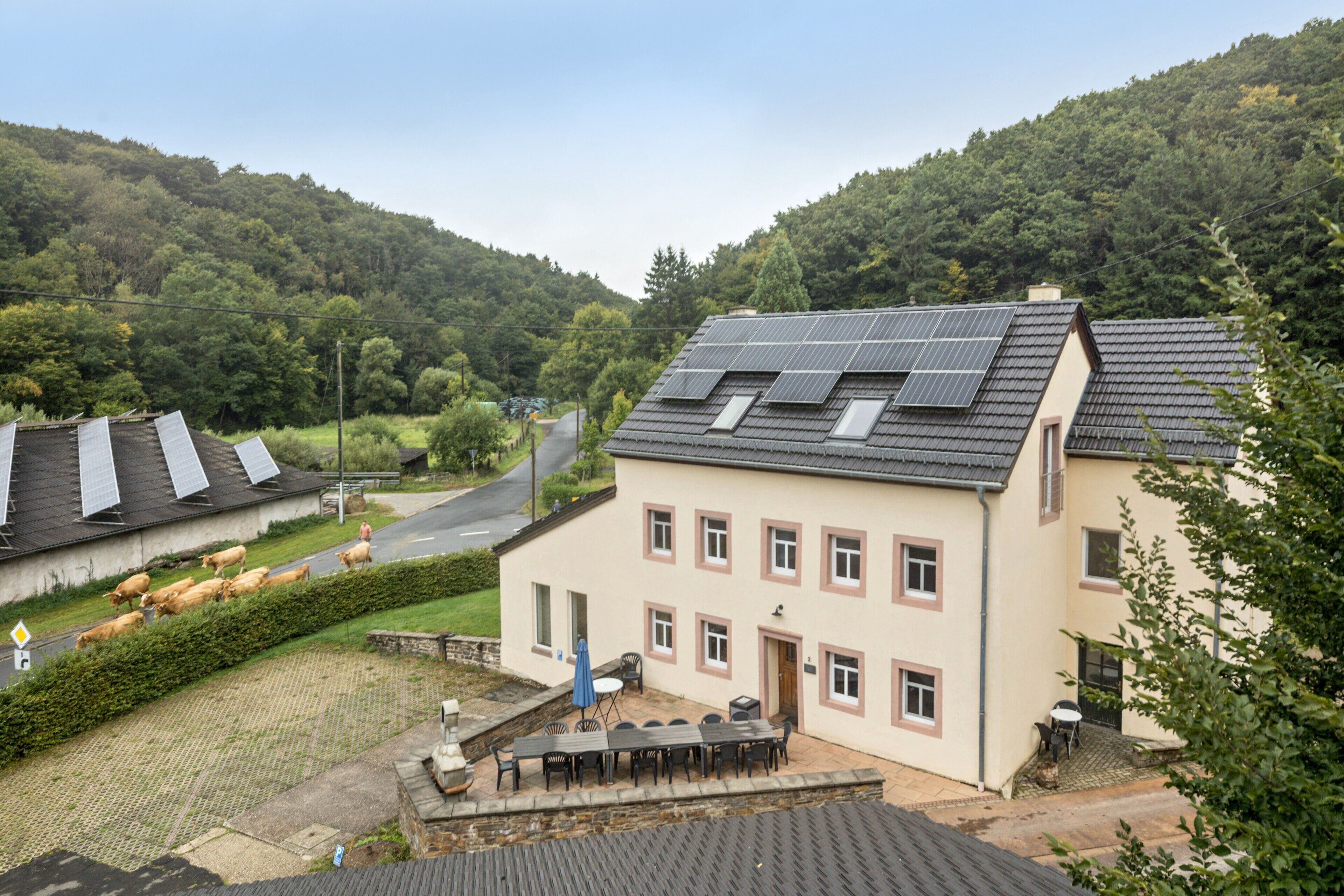 A building with solar panels, a patio with outdoor seating, and a view of a green hillside.