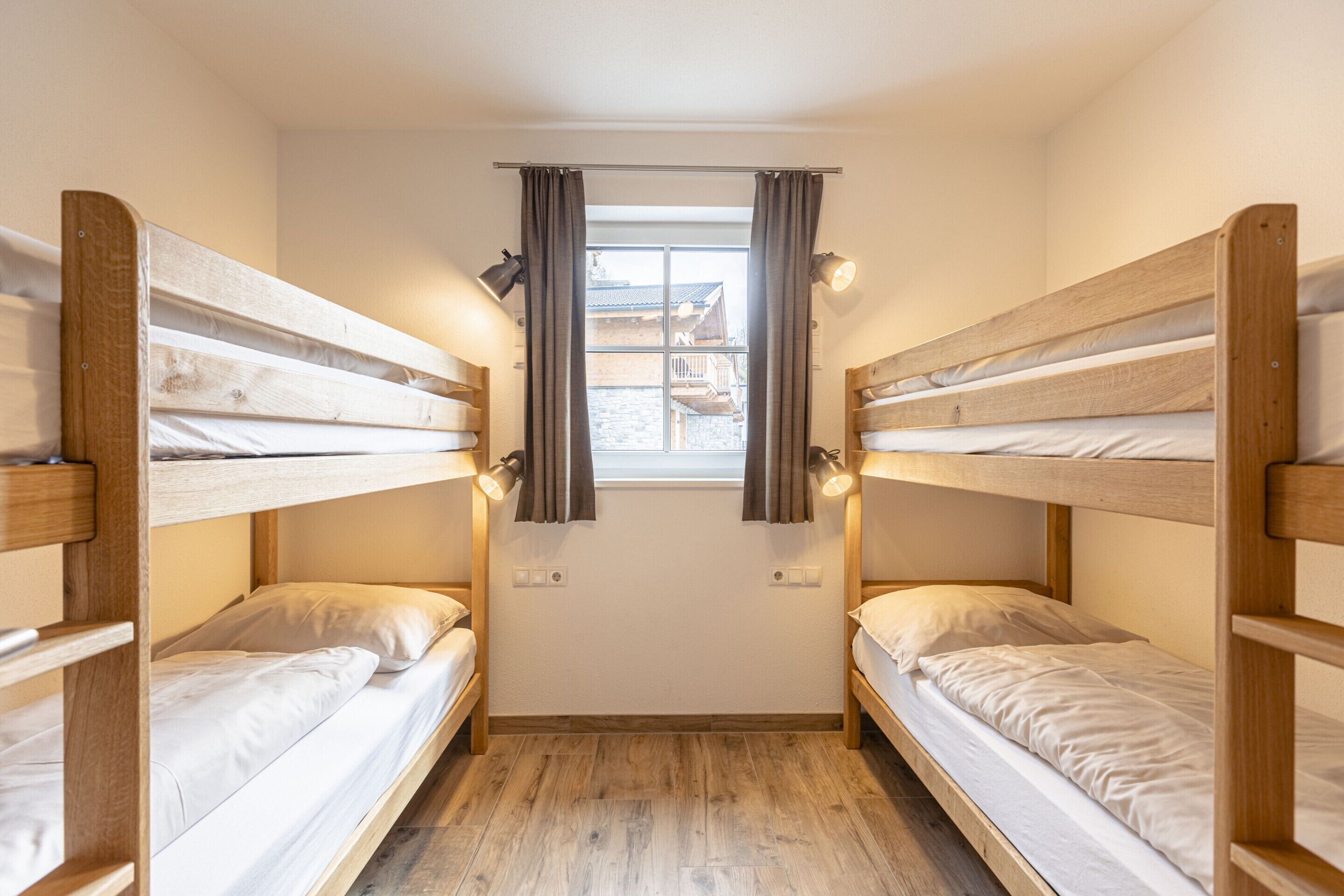 Una habitación pequeña y acogedora con dos literas, una ventana con cortinas y vistas a un edificio.