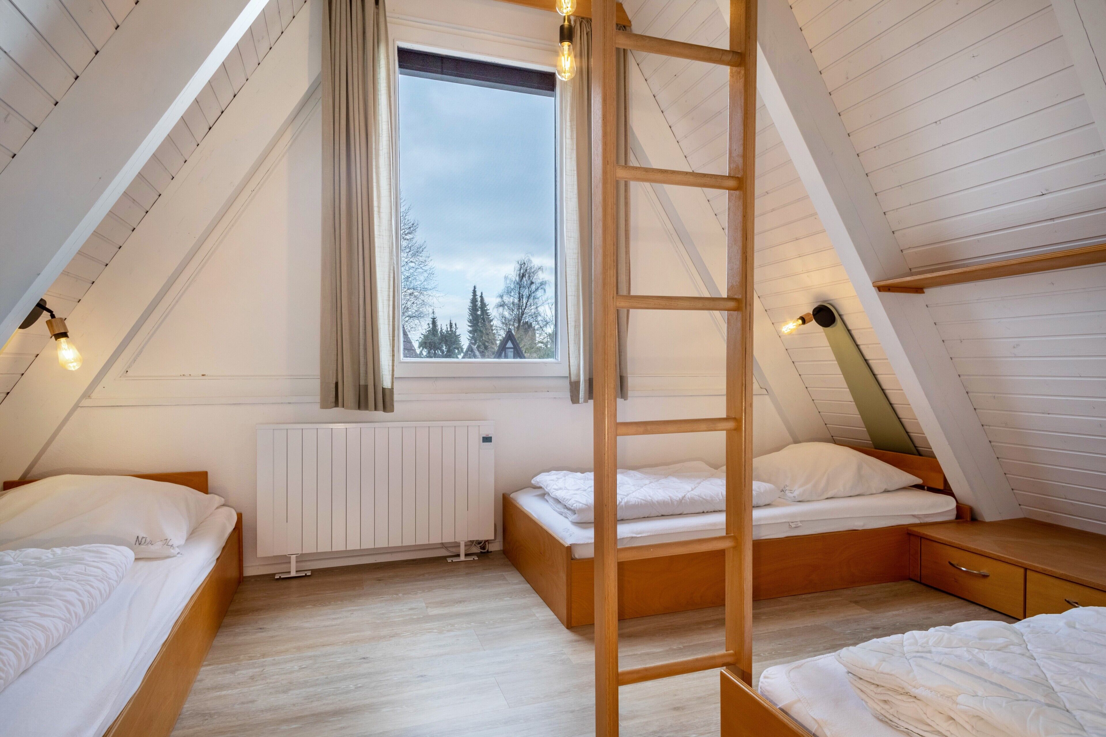 Une chambre de type dortoir, avec des lits superposés, une échelle, une fenêtre donnant sur un paysage agréable et un radiateur.