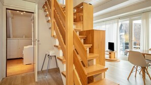 A modern interior with a wooden staircase, a dining area, and a view through a large window.