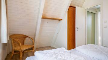 A bedroom with a bed, a wooden chair, a slanted ceiling, and a door.