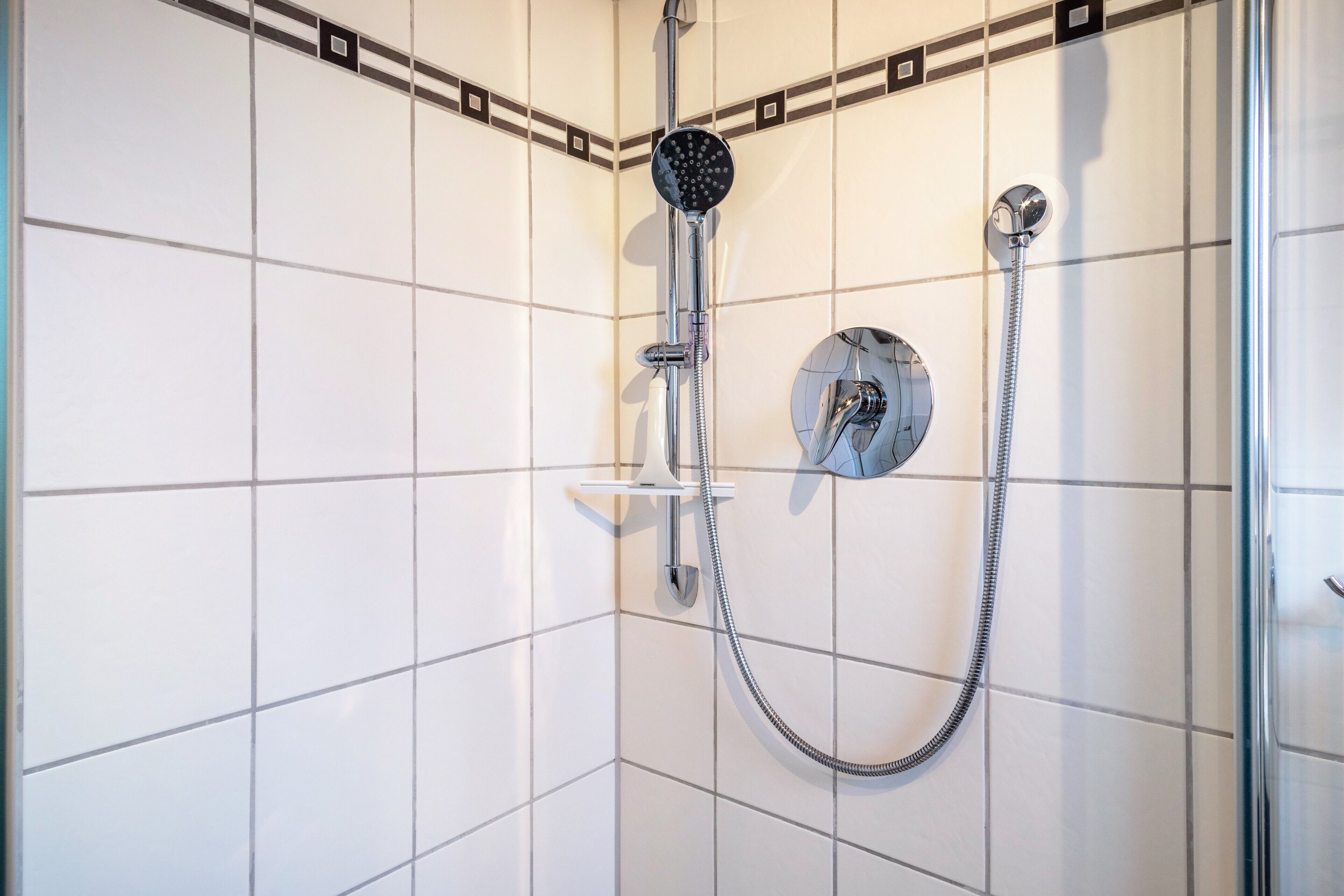A shower with a handheld showerhead and a wall-mounted faucet.