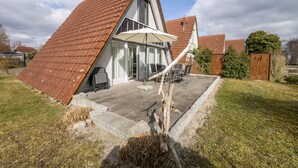 A house with a sloped roof, a patio with outdoor furniture, and a garden area.