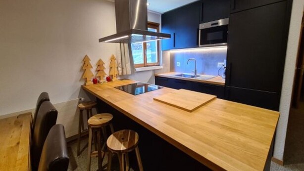 Een moderne keuken met een houten kookeiland, barstoelen, een roestvrijstalen afzuigkap en donkere kasten.