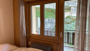 Een slaapkamer met een groot bed, houten wanden, een radiator en een glazen schuifdeur die leidt naar een buitenbalkon.
