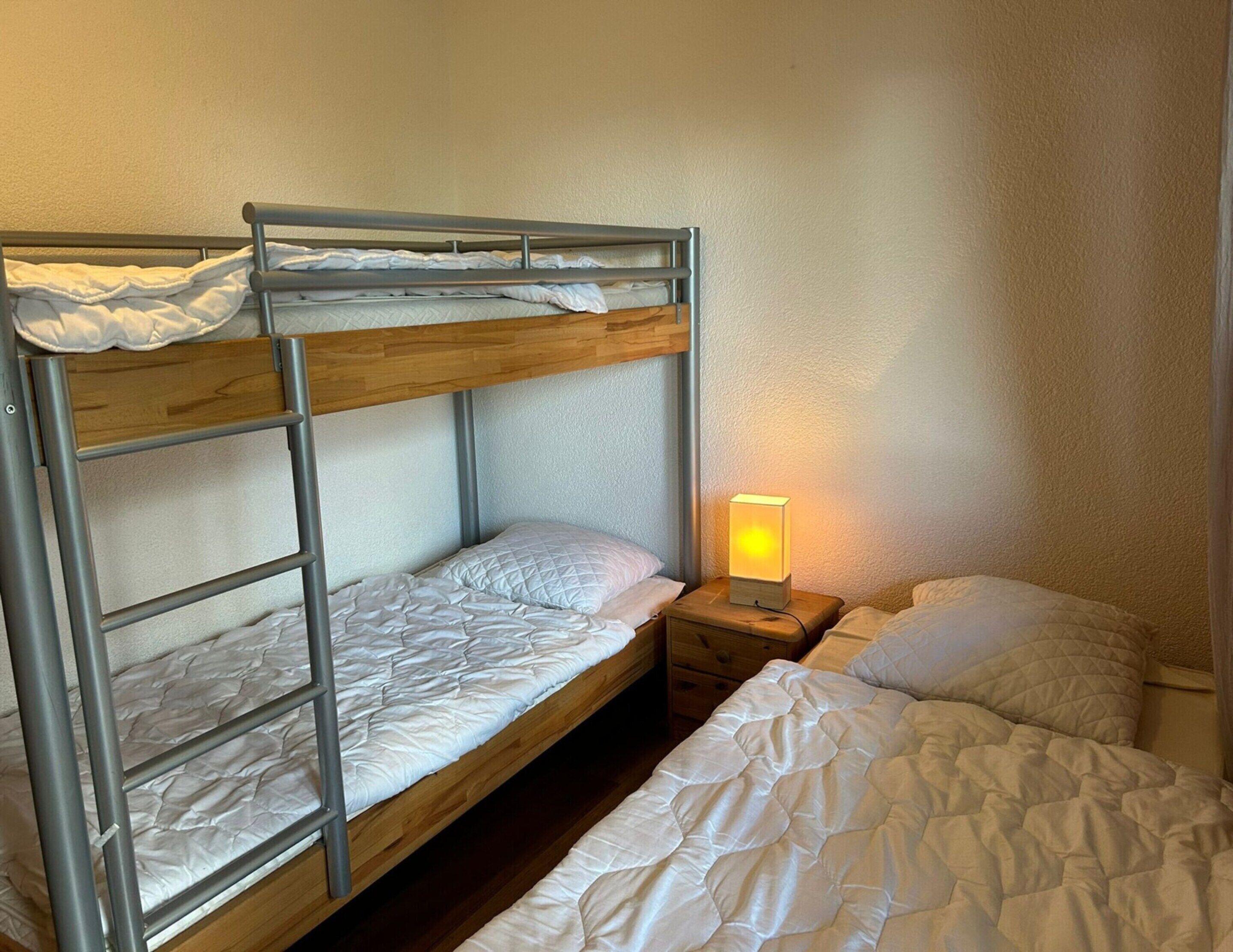Habitación con literas, mesita de noche y lámpara de mesa.