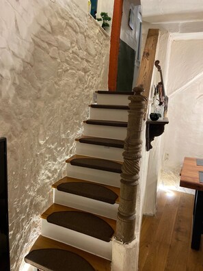 A spiral staircase with a wooden handrail and steps, leading to a landing with a wooden table and a vase of flowers.