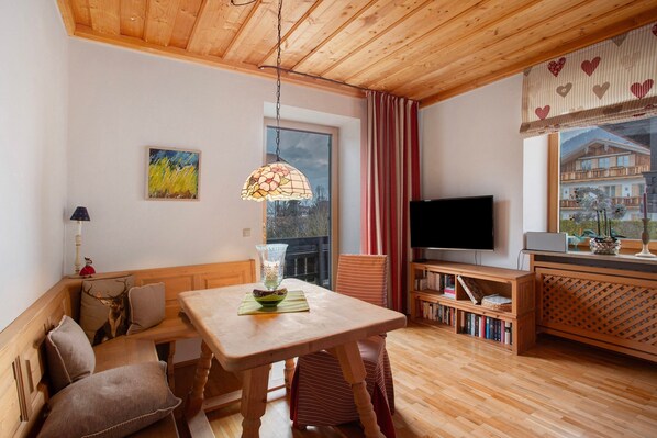A cozy room with a wooden ceiling, a dining table, a bench, a TV, and a bookshelf.