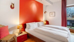 Un dormitorio con una cama grande, dos mesitas de noche, una mesita auxiliar, una pared roja y una ventana con vistas.