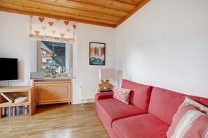 A living room with a red sofa, wooden flooring, a TV, a window with a view, and a painting on the wall.