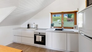 Una cocina moderna con armarios blancos, horno integrado, lavamanos y ventana con vistas al verdor.