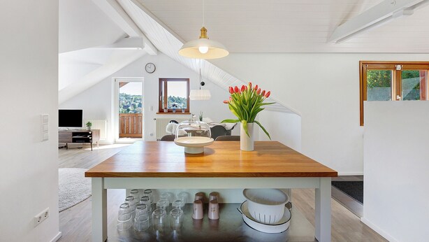 Una cocina moderna con una isla de madera, paredes blancas y un amplio ventanal.