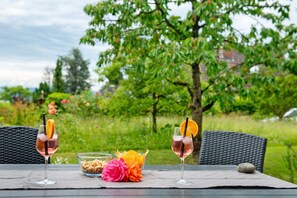 Two glasses of pink beverage with orange slices on a table with a wicker chair, a bowl of nuts, and a flower. - Holiday Apartment 'With Garden View' (Uhldingen-Mühlhofen)
