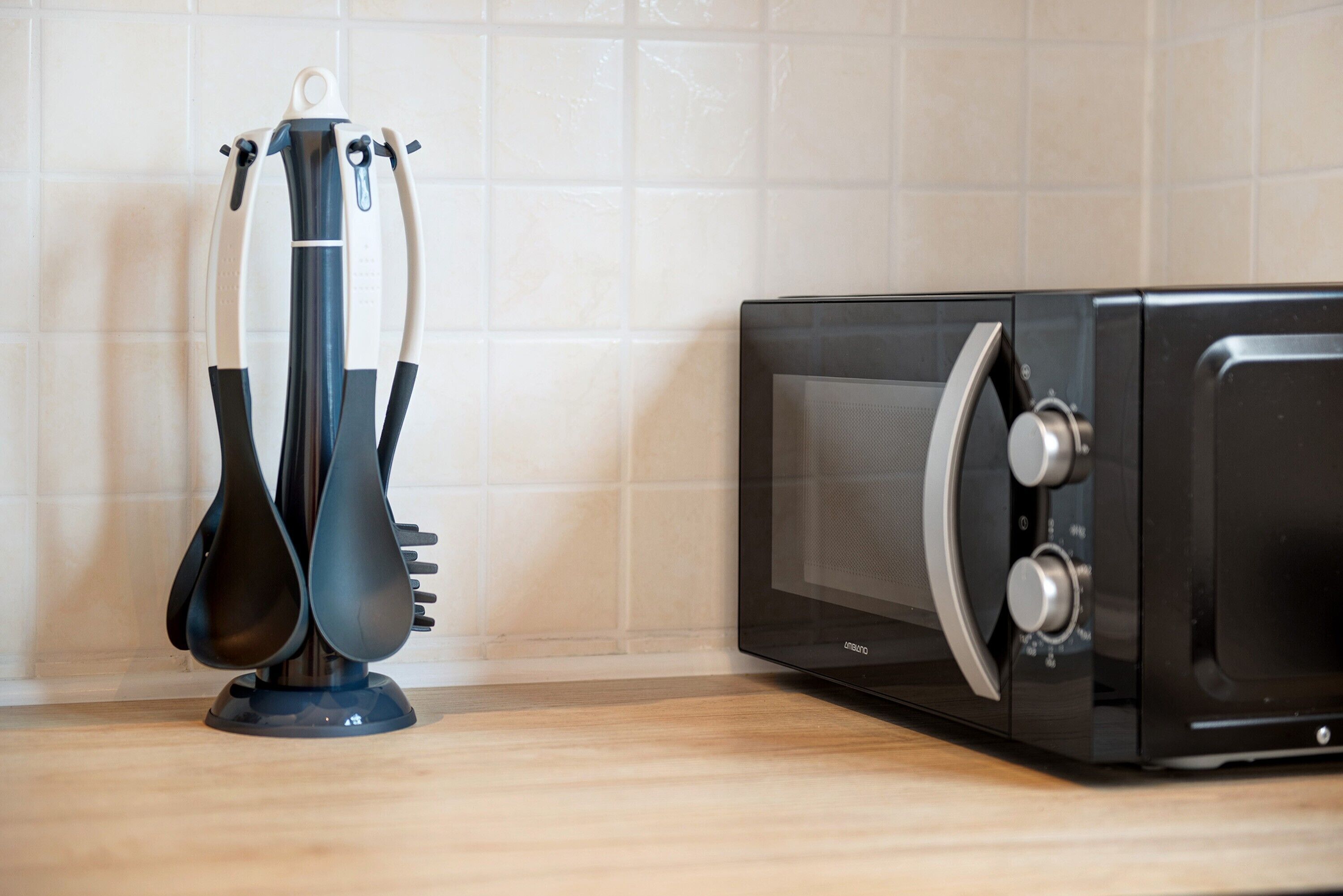 Un four à micro-ondes et une bouilloire noire sont posés sur un plan de travail de cuisine, avec un dosseret de carreaux blancs.