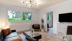 A modern living room with a sofa, coffee table, TV, and a dining area with a table set for two.