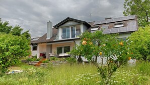 A house with solar panels, a balcony, and a garden with flowers.