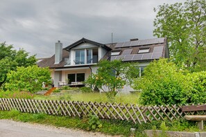 Una casa de dos pisos con techo inclinado, paneles solares y una cerca de madera.