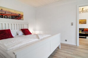 A bedroom with a white bed, red pillows, a painting of a pier, and a wooden floor. - Holiday Apartment 'With Garden View' (Uhldingen-Mühlhofen)