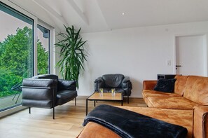 Un salon moderne avec un canapé, un fauteuil, une table basse et une grande plante.
