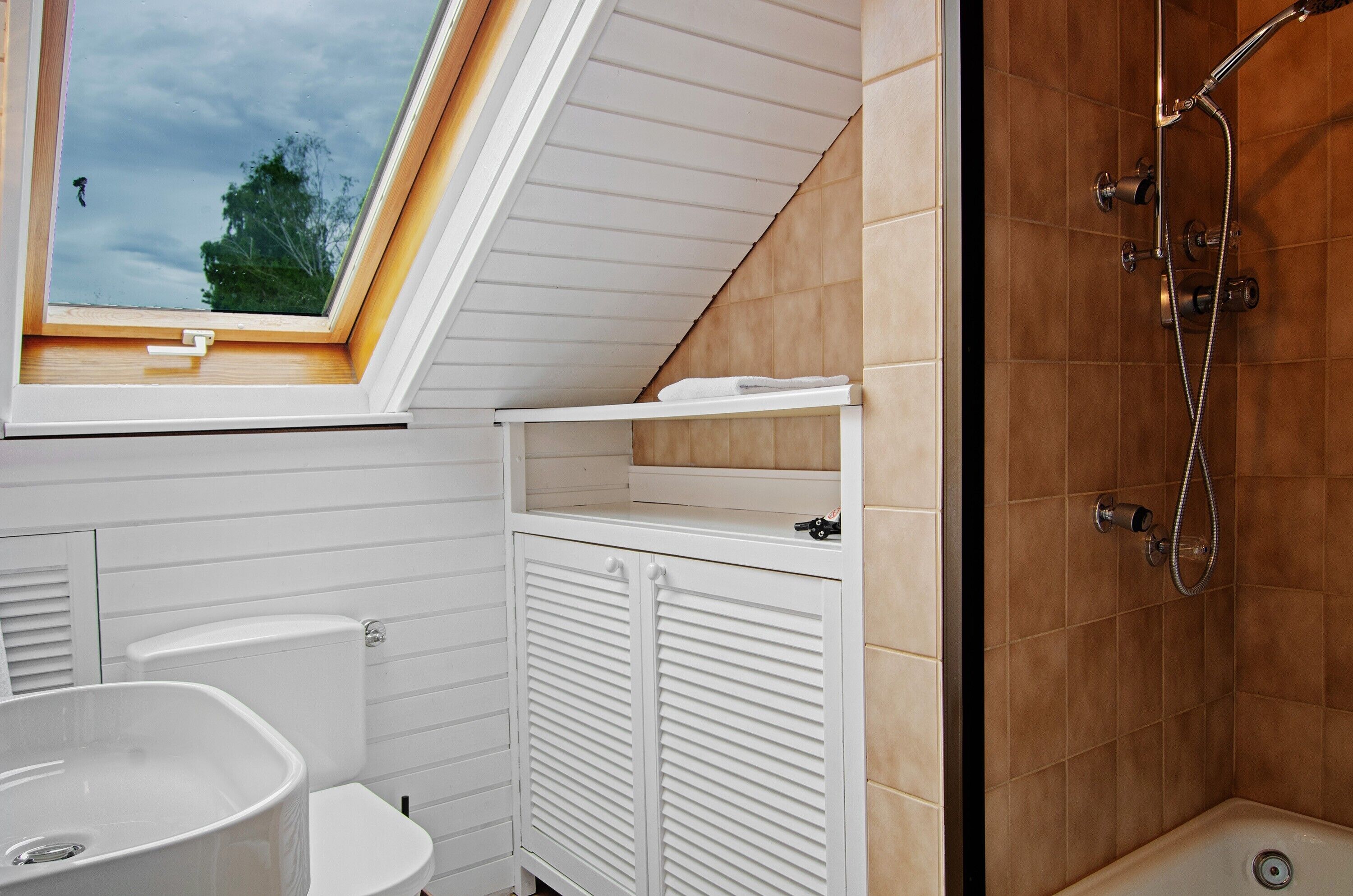 Ein Badezimmer mit Oberlicht, Dusche, Toilette und Waschbecken.