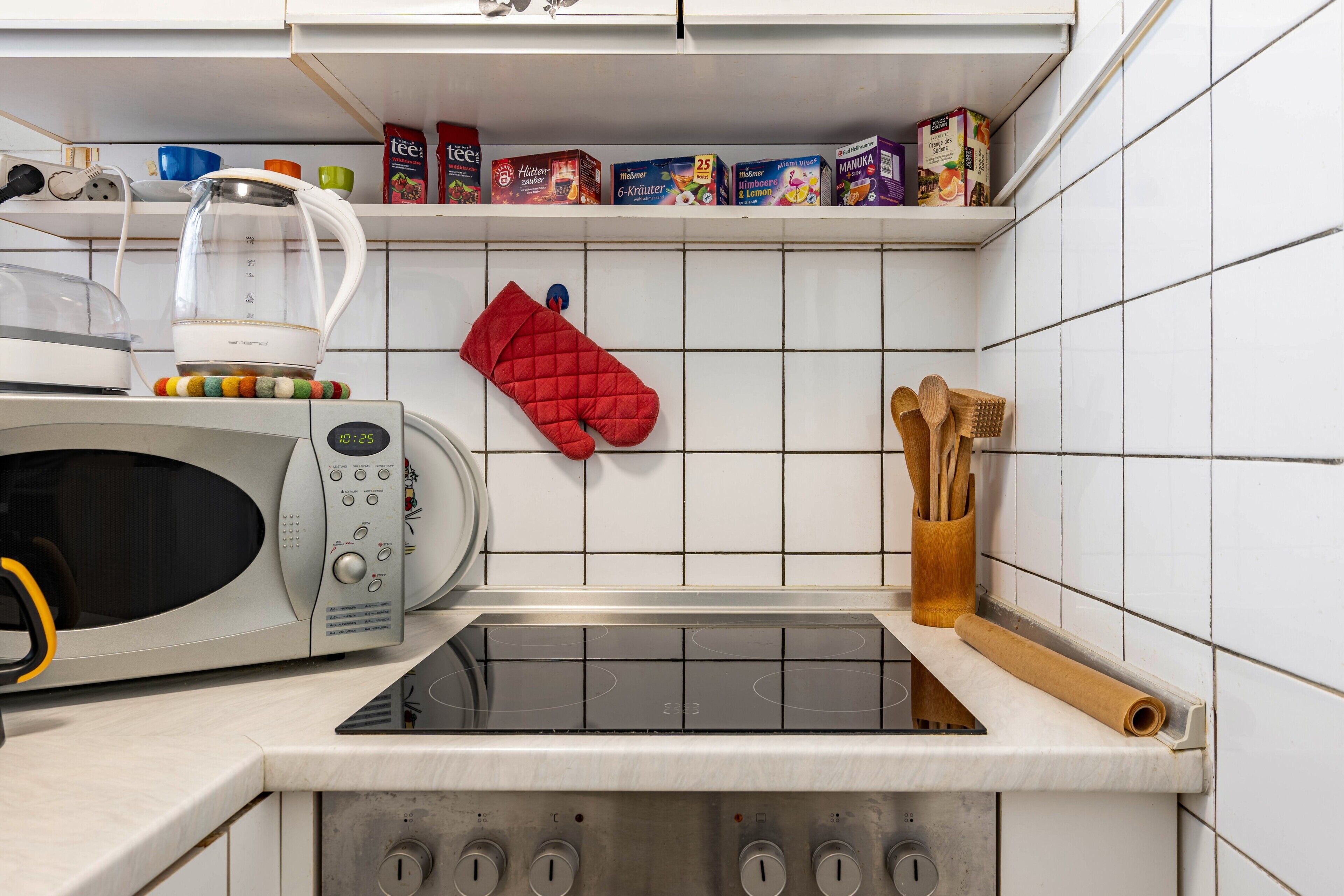 Une cuisine équipée d’un four à micro-ondes, d’une bouilloire et d’un manique rouge accroché au mur.