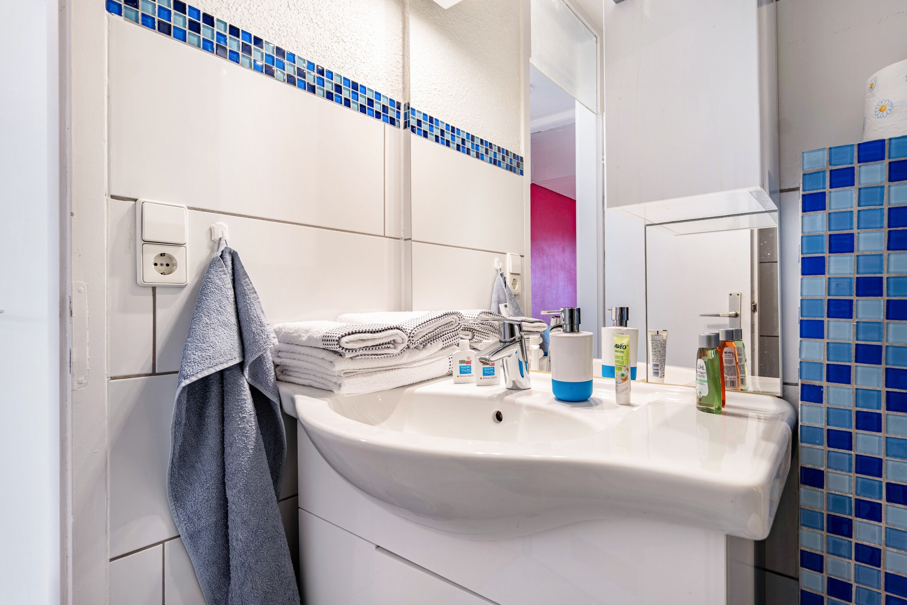 A bathroom with a white sink, a mirror, a towel rack, and a blue-tiled wall.