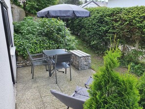 Une terrasse extérieure avec une table et des chaises, un banc en pierre et un grand parasol.