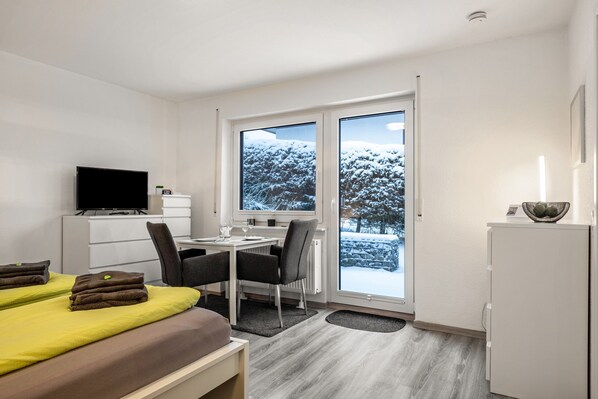 Une chambre d’hôtel avec un lit, un bureau, une chaise, une télévision et une vue sur un paysage enneigé par la fenêtre.