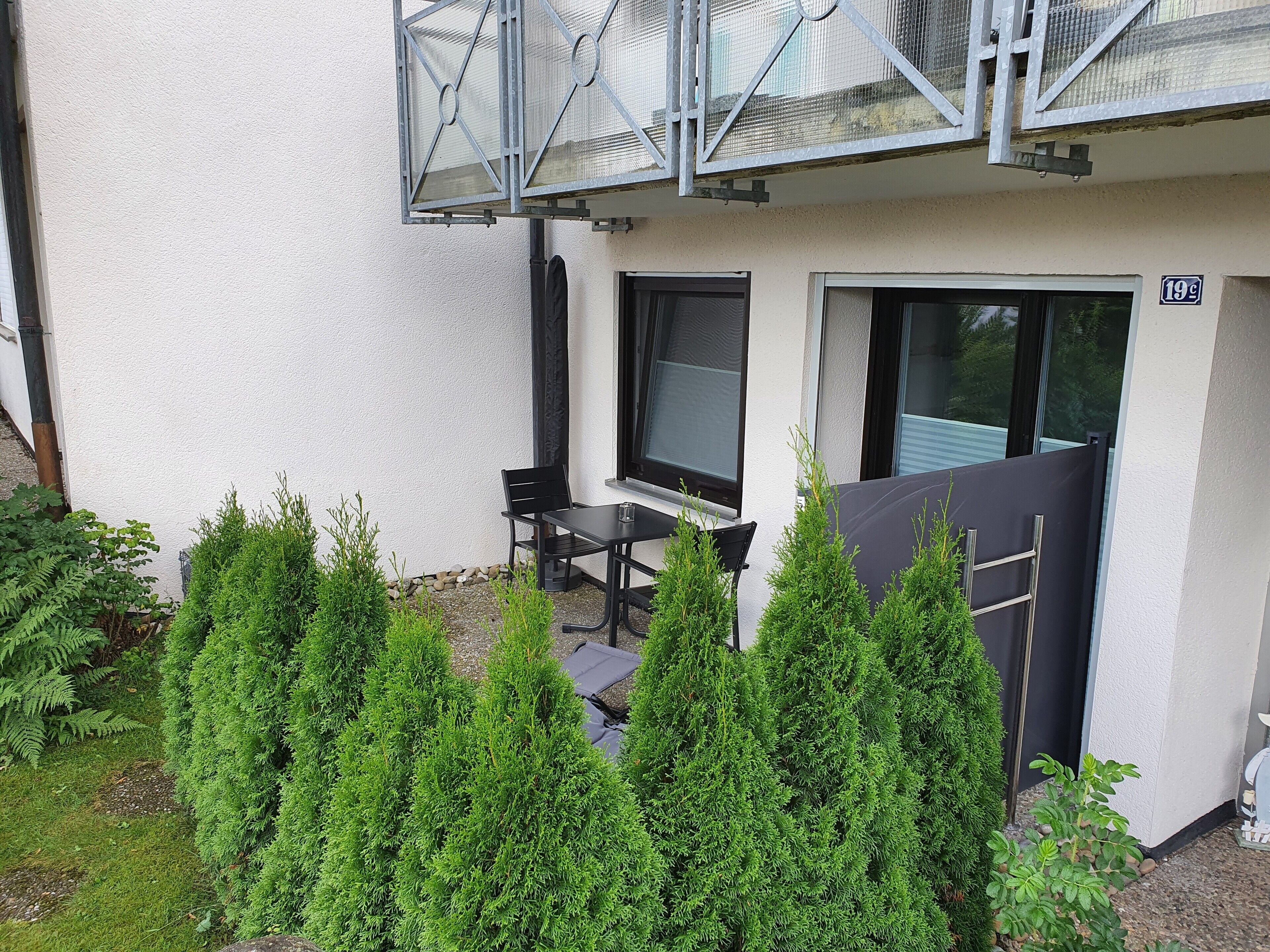 An outdoor seating area with a table and chairs, surrounded by greenery.
