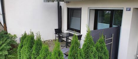 An outdoor seating area with a table and chairs, surrounded by greenery.