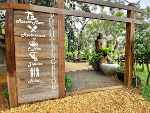 A wooden signboard with amenities listed for a resort, including a restaurant, coffee, zipline, and toilet facilities.