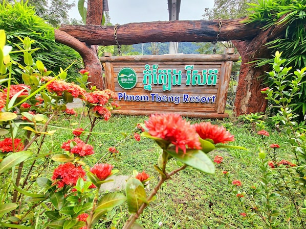 A sign for Phnom Theng Resort surrounded by lush greenery and red flowers.