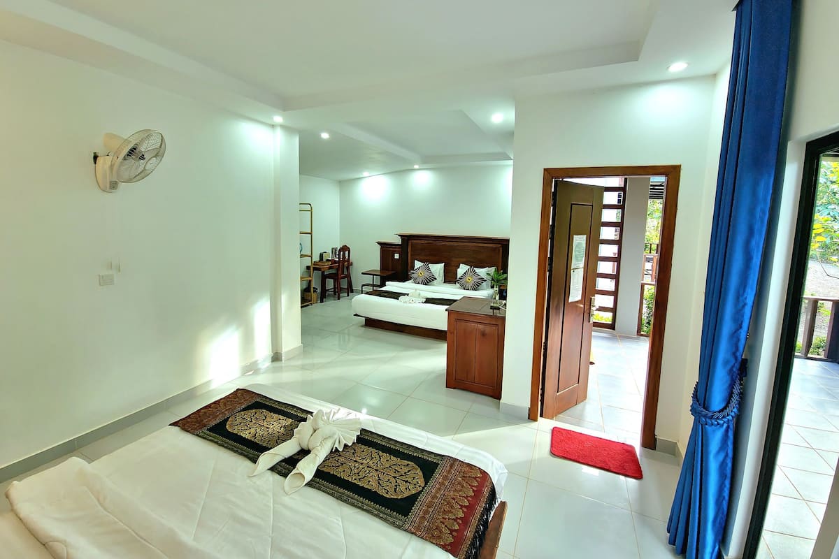 A hotel room with a bed, a desk, a chair, and a wardrobe. There is a door leading to another room.