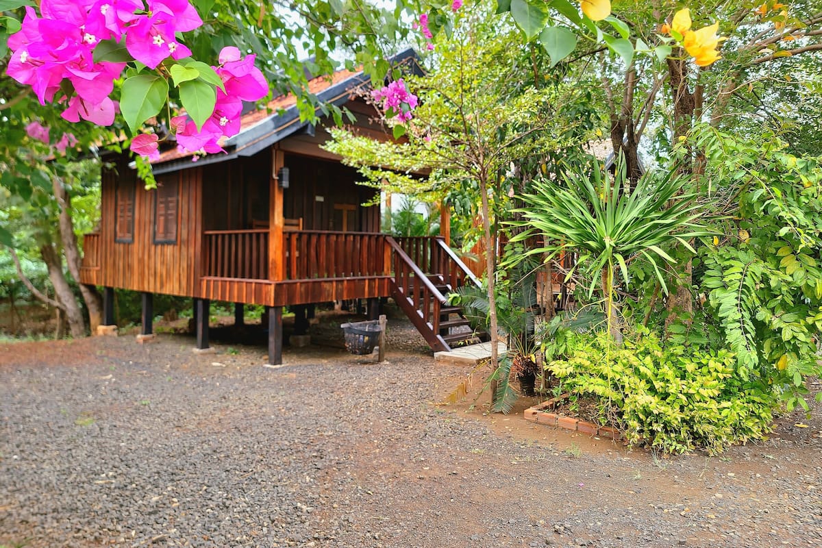 A wooden cabin with a porch, surrounded by lush greenery and vibrant flowers.